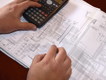 Man using a calculator reviewing electrical design blueprint